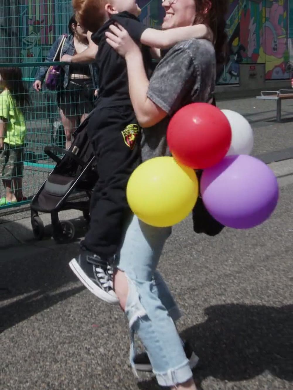 Child being lifted up holding balloons at an outdoor baby rave in Vancouver.