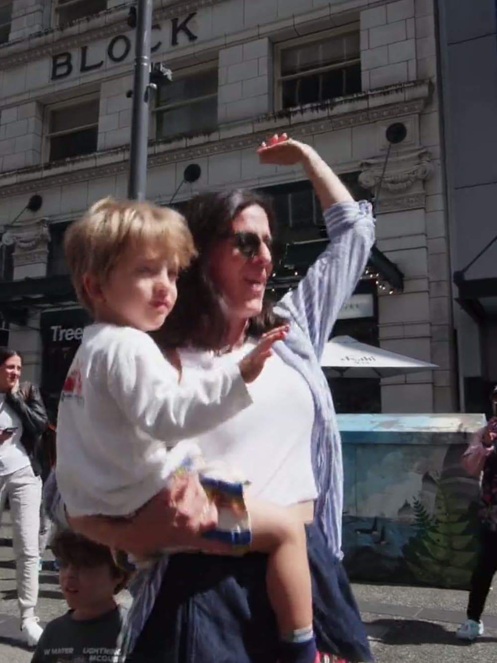 Parent carrying a small child at an outdoor baby rave in downtown Vancouver.