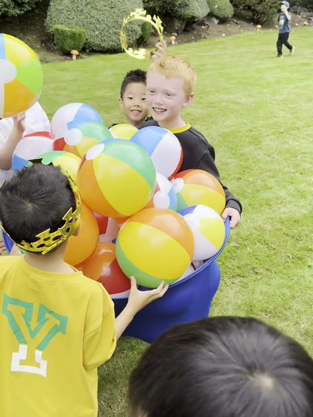 Boy carrying an armful of beach balls back to his team on the grass at a Vancouver party.