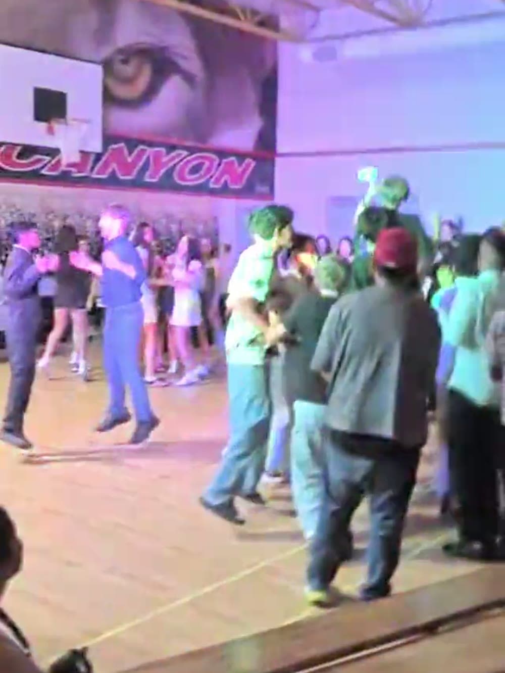Students dancing under coloured lighting and glow sticks in a school gym.