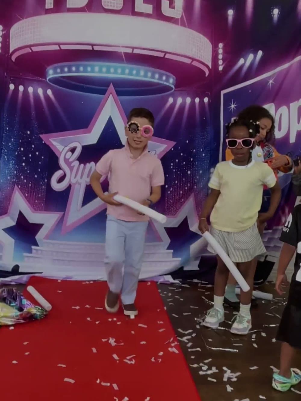 Kids walking a red carpet in sunglasses under a stage backdrop at a Vancouver party.