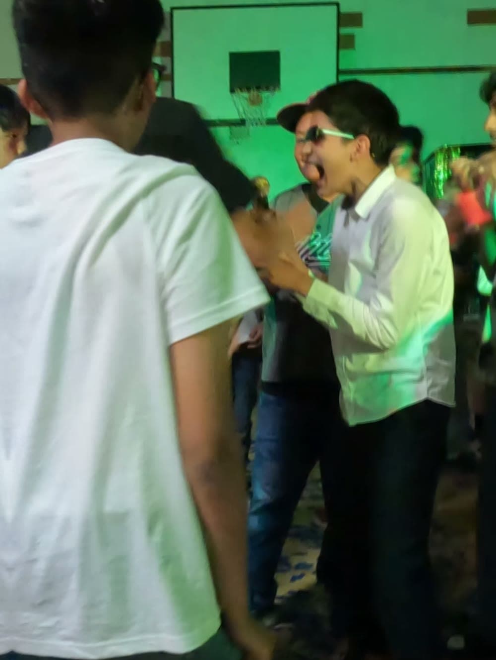 Student singing along with a friend under green lighting at a school dance.