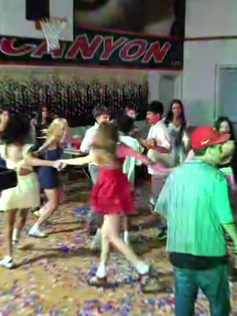 Students dancing on a gym floor covered in confetti at a school dance.